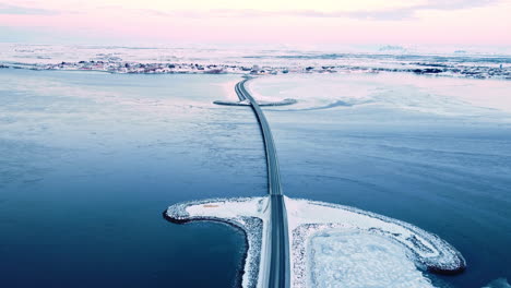 Islandia-Invierno-Paisaje-Cubierto-De-Nieve-Con-Puente-De-Carretera-Cruzando-La-Isla-Al-Atardecer-Imágenes-Aéreas