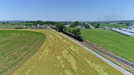 A-historic-steam-locomotive-powers-along-the-tracks,-past-golden-fields,-under-a-clear-blue-sky