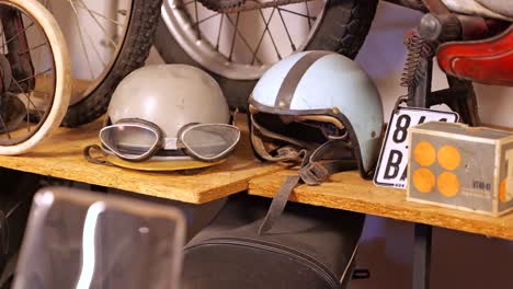 Close-up-of-two-vintage-motorcycle-helmets,-goggles,-on-shelf-in-museum