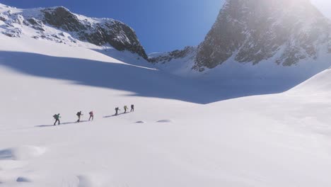 Eine-Aufschlussreiche-Luftaufnahme-Zeigt-Eine-Gruppe-Von-Bergsteigern,-Die-Im-Sonnenlicht-Bergauf-Schneebedeckte-Berge-Wandern