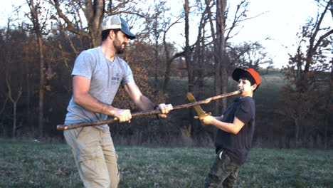 Father-and-son-engage-in-playful-sword-fight-with-sticks-in-the-woods-at-dusk,-showing-family-bonding