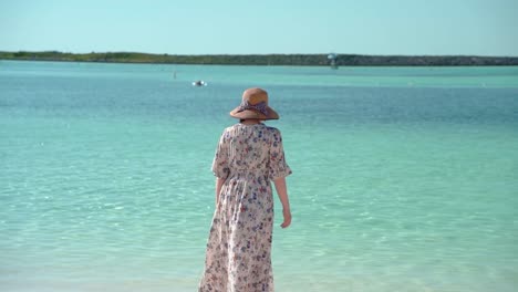 Woman-wearing-a-hat-and-a-dress-turns-around-and-see-beautiful-sea-slow-backshot