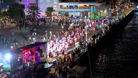 Carnaval-Gran-Marcha-performers-parade-along-shimmering-waterfront-at-night