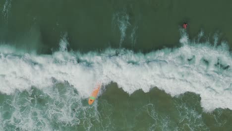 Un-Surfista-Aficionado-Cae-Mientras-Intenta-Montar-Una-Ola-En-Una-Playa-De-Aguas-Verdes-Transparentes,-Mostrando-Los-Desafíos-Y-La-Emoción-De-Aprender-A-Surfear