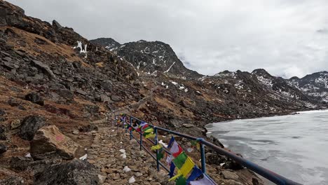 Hiking-path-with-tibetan-prayer-flags-and-a-railing-on-the-shore-of-Cold-and-majestic:-Ice-rocks-and-freezing-waters-capture-the-essence-of-the-Himalayas-at-Gosainkunda