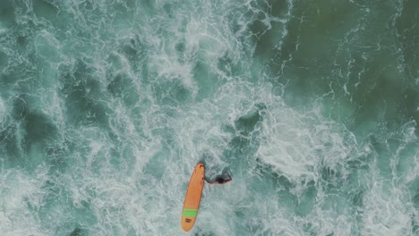 Ein-Surfer-Kämpft-An-Einem-Wunderschönen-Strand-Mit-Kristallklarem,-Grünem-Wasser-Gegen-Die-Wellen