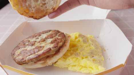 Frühstückssandwich-Und-Omelett-In-Pappschale,-Hand-Nimmt-Brotscheibe-Und-Legt-Sie-Auf-Veganes-Patty
