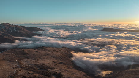 Amanecer-Sobre-Montañas-Con-Nubes-Que-Fluyen-Como-Un-Río-En-El-Valle,-Vista-Aérea,-Timelapse