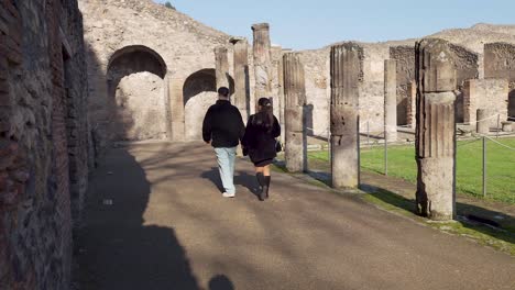 Traveling-Couple-Walking-Past-Stone-Columns-At-Gladiators-Barracks-In-Pompeii,-Italy