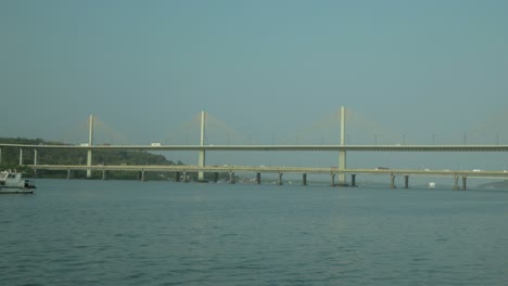 Plano-Amplio-De-Un-Puente-Sobre-Un-Río-Con-Un-Yate-Pasando-Por-Debajo-A-La-Luz-Del-Día.