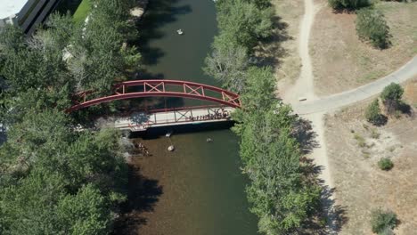 Kreisende-Drohnenaufnahmen-Von-Menschen,-Die-Von-Einer-Roten-Brücke-In-Den-Boise-River-Springen