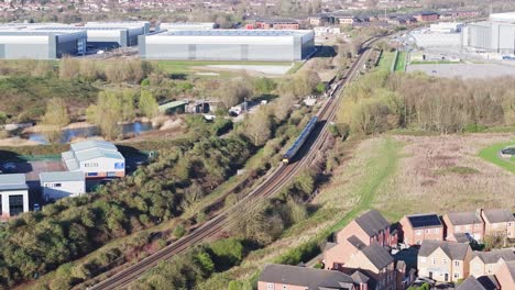 A-top-view-of-a-cinematic-passenger-train-moving-along-the-warehouses-on-a-curvy-railroad-in-Debry,-UK