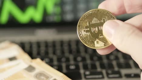 Closeup-shot-white-fingers-play-with-bitcoin-golden-coin-cryptocurrency-chart-green-graphic-going-up,-laptop-background,-screen-with-Euro-paper-cash-bills