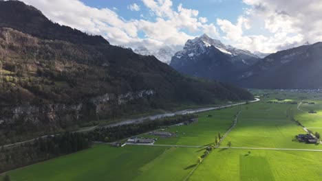 Aerial-view-of-majestic-mountain-view-surrounded-by-clouds-in-a-sky-at-Walensee-Wessen,-Switzerland,-snowy-mountains-and-greenery