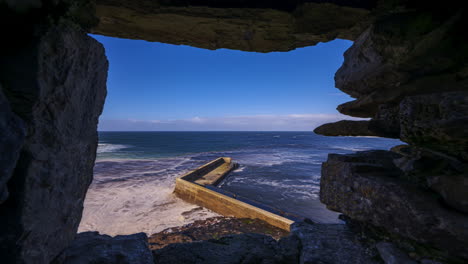 Time-lapse-of-concrete-block-pier-viewed-from-above-through-a-medieval-stone-castle-window-on-sunny-cloudy-day-located-in-Easkey-county-Sligo-along-the-Wild-Atlantic-Way-in-Ireland