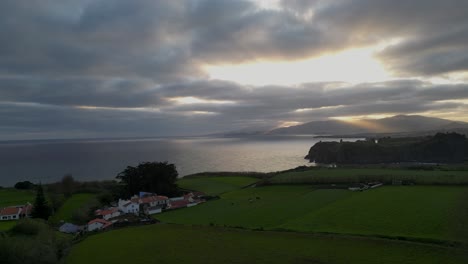 Aerial-Scenic-View-Of-Sunbeam-Falling-In-Sea-During-Sunset,-Drone-Flying-Over-Filed-On-Cliff---Azores,-Portugal