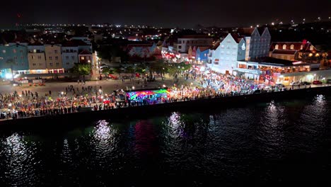 Shining-parade-lights-reflect-on-Caribbean-waters-with-multicolored-buildings-at-night