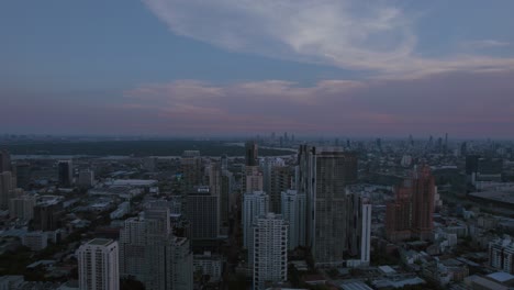 Dusk-settles-over-Bangkok’s-cityscape,-blending-modern-skyscrapers-with-traditional-buildings-under-a-pastel-sky