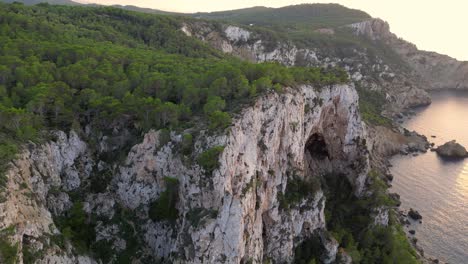 Wanderer-Ruhen-Sich-Auf-Einer-Felsklippe-Zwischen-Bäumen-Aus-Und-Haben-Bei-Sonnenuntergang-Auf-Ibiza-Blick-Auf-Die-Grüne-Landschaft