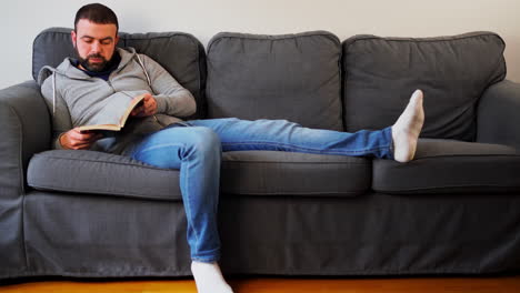 Mann-Liest-Buch,-Während-Er-Auf-Der-Couch-In-Seiner-Wohnung-Sitzt