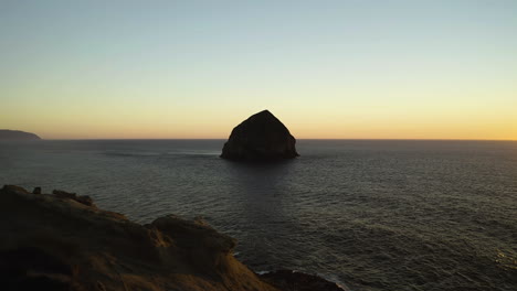 Luftaufnahme-über-Sandsteinfelsen-Zum-Haystack-Rock-Mit-Sonnenuntergang-In-Der-Mitte,-Küste-Oregons