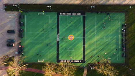 Aerial-top-down-of-people-playing-soccer-and-basketball-on-three-green-sport-fields-during-sunset