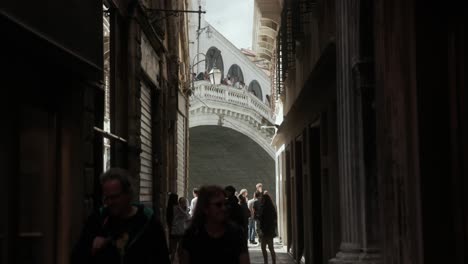 Gente-Caminando-Por-Un-Callejón-Con-El-Puente-De-Rialto-Al-Fondo-En-Venecia,-Italia