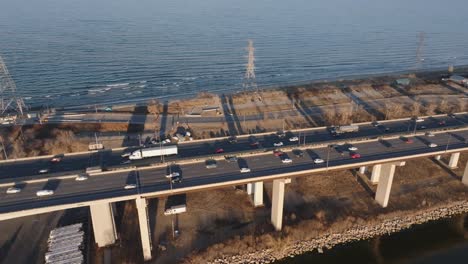 A-busy-highway-by-the-lake-in-Hamilton,-Ontario-during-golden-hour,-light-traffic,-aerial-view