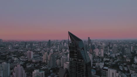 Desde-Un-Punto-De-Vista-Aéreo,-El-Horizonte-De-Bangkok-Se-Despliega,-Mostrando-La-Vida-Urbana-Sobre-Un-Fondo-Donde-El-Horizonte-Adquiere-Tonos-De-Rojo-Y-Violeta-Después-Del-Atardecer.