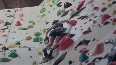 Mujer-Joven-Practicando-Escalada-En-Roca-En-Una-Pared-De-Roca-En-El-Interior.