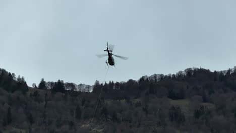 A-helicopter-hovers-above-the-forests-of-Switzerland,-demonstrating-aerial-operations-in-woodland-environments-and-various-tasks-involving-ropes