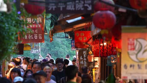 Large-crowds-of-people-strolling-through-narrow-laneway-lined-with-food-stalls-and-souvenir-shops,-exploring-the-bustling-Jiufen-Old-Street-of-the-mountain-town,-popular-tourist-attraction-of-Taiwan