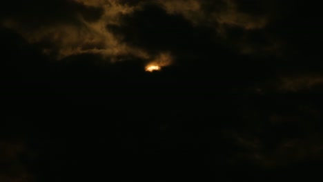 Dramatic-dark-clouds-revealing-bright-glowing-moon-at-night,-telephoto