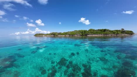 Crystal-clear-turquoise-waters-near-a-tropical-isle,-with-lush-greenery-under-a-sunny-sky,-serene-ambience