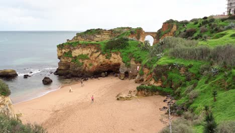 Una-Hermosa-Playa-De-Arena-Suave-Con-Exuberantes-Acantilados-Verdes-Y-Espectaculares-Formaciones-Rocosas-En-Lagos,-Algarve,-Portugal