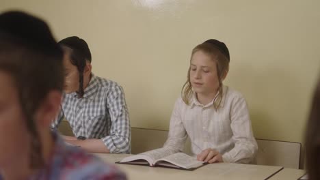 ultra--Orthodox-Jewish-students-with-a-kippahs-lerning-in-class,-looking-in-a-jewish-book