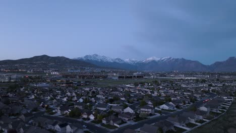 Suburb-in-a-valley-beneath-snow-capped-mountains-at-dusk---aerial-flyover