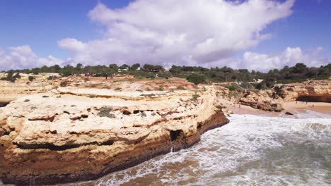 Coastline-view-with-beach-cove-transitioning-to-orange-rugged-cliffs-with-groups-of-hikers-and-a-natural-wave-carved-arch-by-aerial-4k-drone-at-Albandeira-beach-in-the-Algarve-region-of-Portugal
