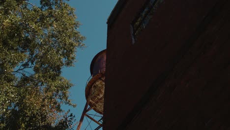 Revelando-Desde-Detrás-De-Un-Gran-Edificio-Y-Una-Antigua-Torre-De-Agua-Oxidada.