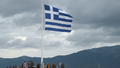 Greek-flag-waving-with-the-wind-in-Athens-with-many-tourists-under-it