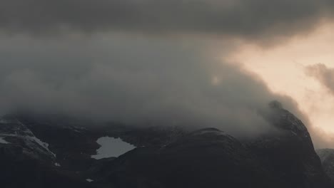 Stormy-clouds-backlit-by-the-sunset-whirl-above-the-snow-capped-mountains-in-the-timelapse-video