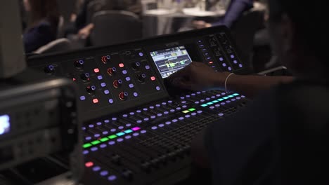 Audio-engineer-operating-a-modern-mixing-console-at-a-live-event,-close-up,-dim-lighting