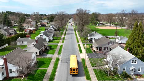 Yellow-American-school-bus-driving-on-street-of-noble-residential-area-in-USA