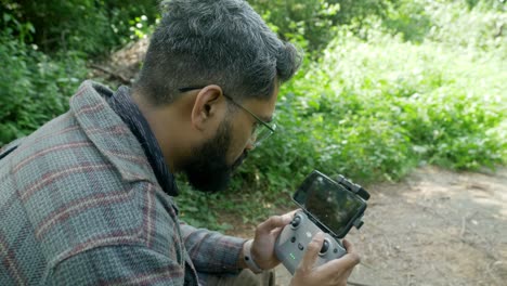 Professional-drone-pilot-using-drone-remote-controller-with-a-smartphone-attached-in-a-forest-landscape