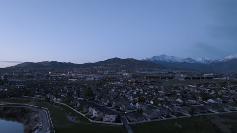 Lehi,-Utah-sits-in-a-valley-beneath-the-Wasatch-Front's-snow-capped-mountains---aerial-flyover-at-twilight
