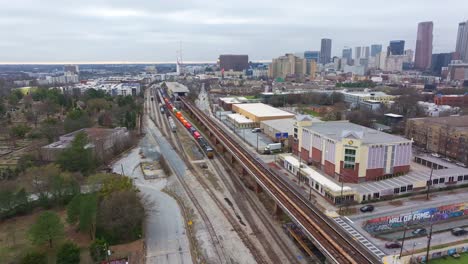 Aerial-of-King-Memorial-subway-station-rail-track,-Husley-shipping-Yard-Beltline-stretch,-Atlanta-Intown-neighborhood-with-Downtown-Atlanta-skyscrapers-in-background