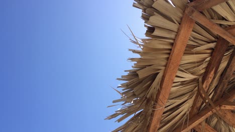 Straw-beach-umbrella-in-slight-breeze,-vacation-under-blue-sky