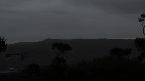 Slow-Sunrise-behind-mountain-on-cloudy-day-with-trees-and-crane,-Gosford-NSW