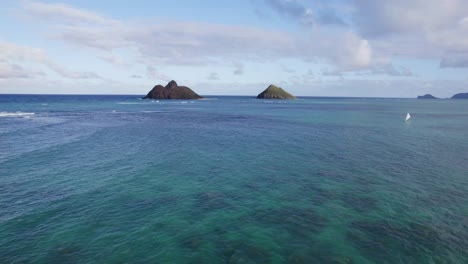 Drone-footage-across-the-clear-ocean-water-toward-two-small-islands-off-the-coast-of-Oahu-Hawaii-near-Lanikai-Beach-with-coral-reefs-showing-through-the-blue-green-water