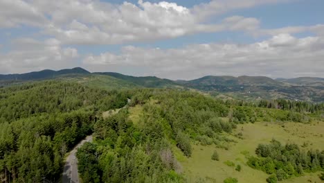 Volando-Sobre-Una-Carretera-Vacía-Rodeada-De-árboles-En-Las-Montañas-Con-Nubes-En-El-Cielo